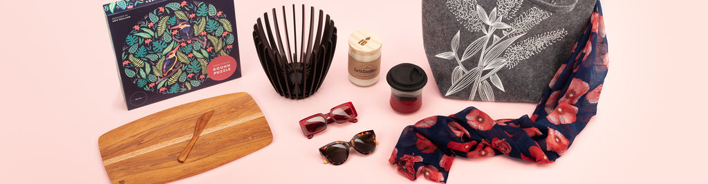 A photo showing a range of lifestyle products sold by Auckland Museum’s store, including poppy printed scarf, round jigsaw puzzle, carved wooden serving platter, sunglasses and Earth Candles