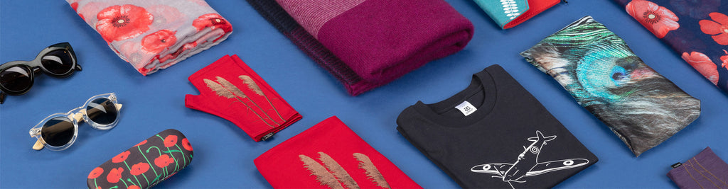 Photo showing a range of clothing and accessories sold by Auckland Museum’s store, including merino fingerless mittens, merino scarf, poppy scarf and Spitfire printed t-shirt