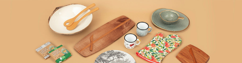 Selection of tableware products sold by Auckland Museum’s store including carved wooden serving platter, pohutukawa oven mitt, reusable lunch wraps and enamel mugs